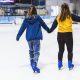 Two women hold hands while skating at an ice rink