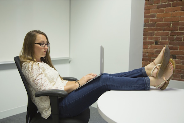 Young woman with laptop and feet on desk