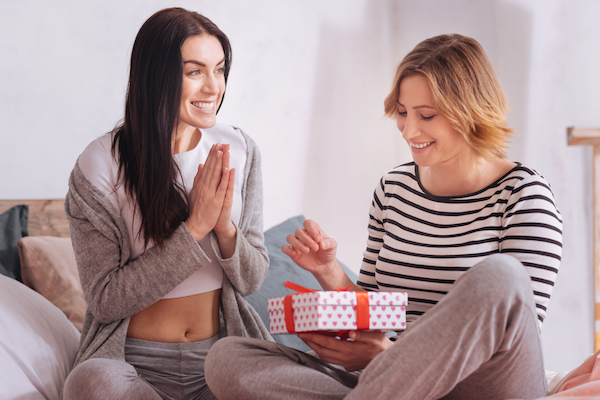 Woman giving girlfriend gift in bed