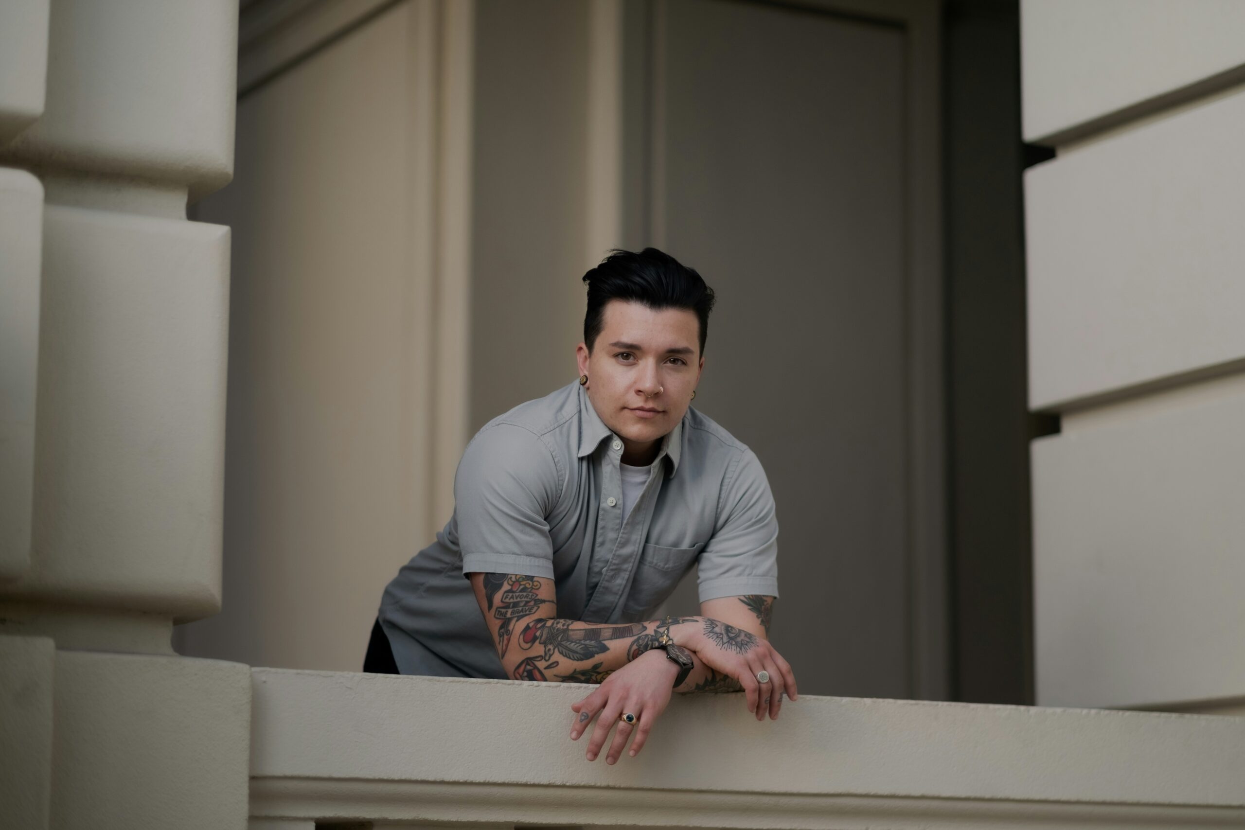 (Photo: Levi Meir Clancy via Unsplash) A person with short slicked back hair and tattoos poses in a sharp button up top.