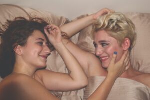 A sapphic couple smile at each other in bed