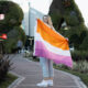 Digital creator and Instagram influencer Allyssa Leaton stands on a path in Buenos Aires, Argentina. She is holding a large lesbian flag which obscures a view of her body. Her head is visible and she smiles into the camera.