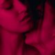 A couple engage in a room bathed in red light. One person sensually kisses the other's neck. The woman being kissed has her eyes closed in bliss.