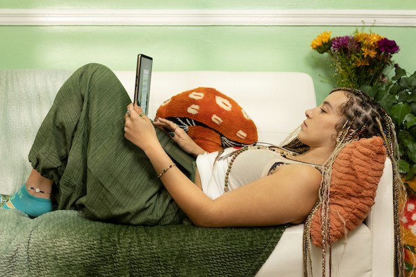 A young woman lies on a couch. In her lap is a laptop that she looks to be working on.