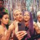 A group of LGBTQ+ people of various ethnicities pose together against a glittering backdrop.