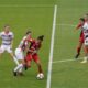 Two women's soccer teams play against one another. One team wears red, the other wears white.