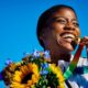 A beautiful Black woman athlete stands holding a gold medal on a rainbow lanyard.