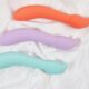 Three vibrators are laid out on a white sheet. The top one is orange, the middle purple, and the bottom a sea foam green.