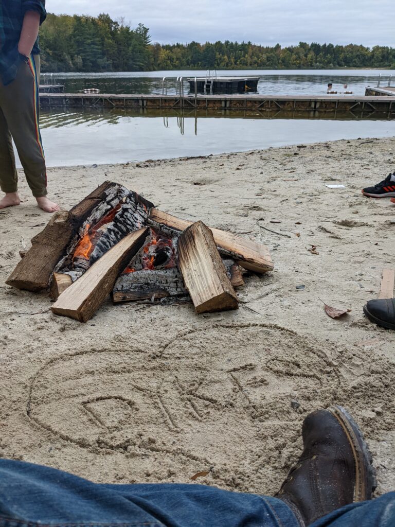 A bonfire on the beach. In the sand, someone has written "DYKES" and encircled it with a heart.