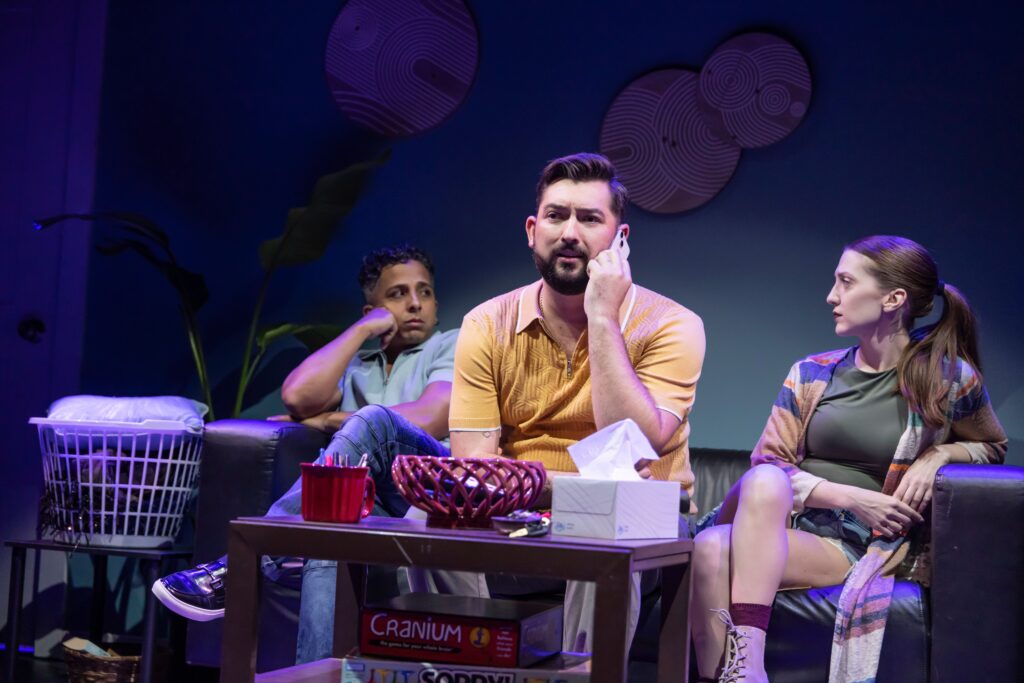 Blake Aburn, and two other actors, sit on a couch as Aburn receives a phone call.