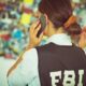 A woman in an FBI vest talks on the phone as she looks at an evidence board.