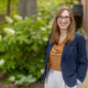 LGBTQ+ candidate for Congress Sarah McBride poses outside near a brick building. She has a welcoming smile on her face.