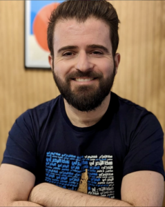 Author Elias Jahshan poses for a portrait. His arms are crossed as he smiles into the camera.