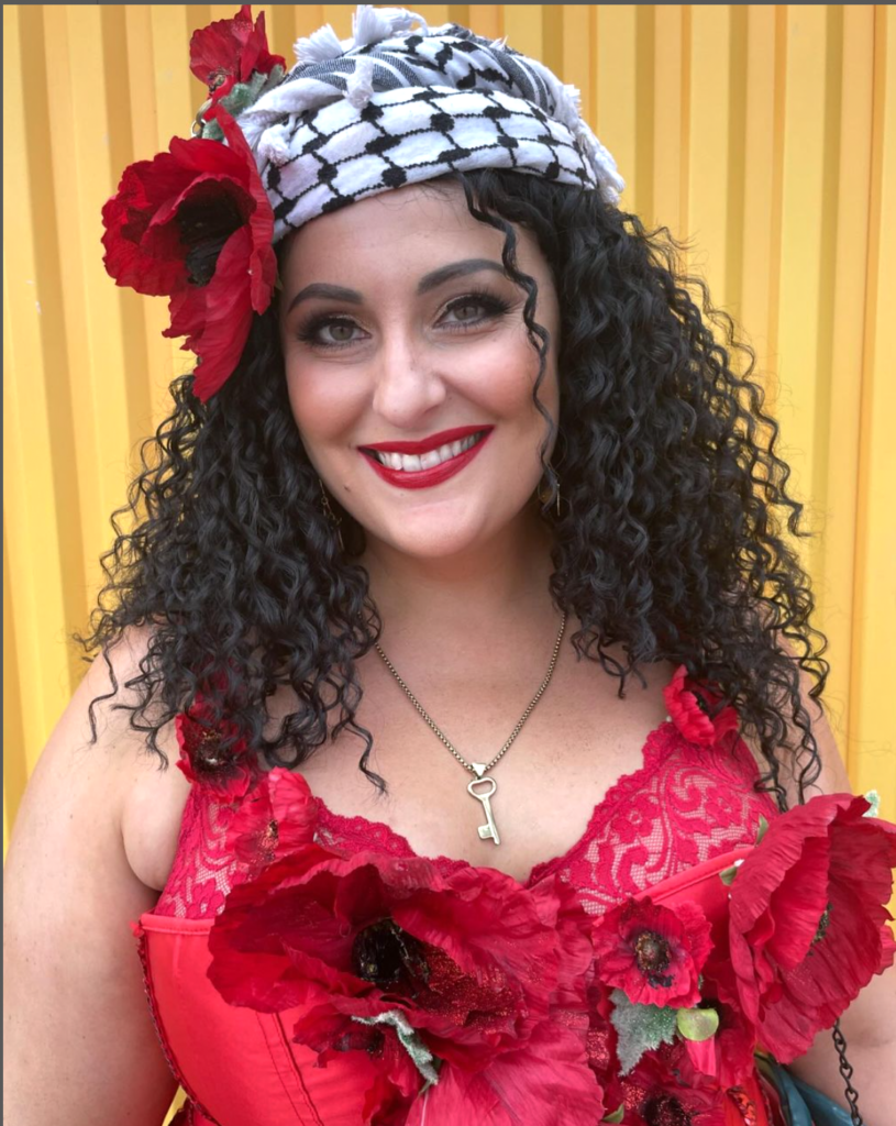 Artist Juliet Orchid poses with a smile, a black and white Keffiyeh wrapped around the top of her head.