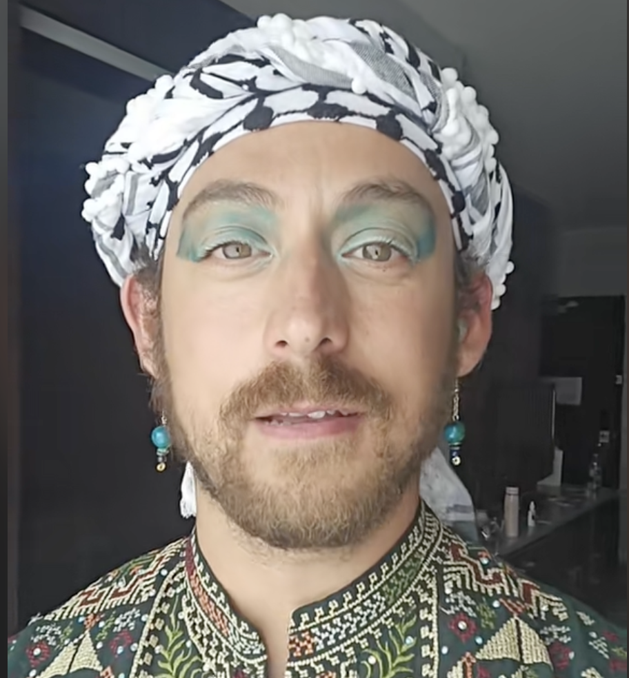 Poet and activist Yaffa As speaks into the camera. They are wearing a black and white keffiyeh around their head and their green eyeshadow matches their earrings.