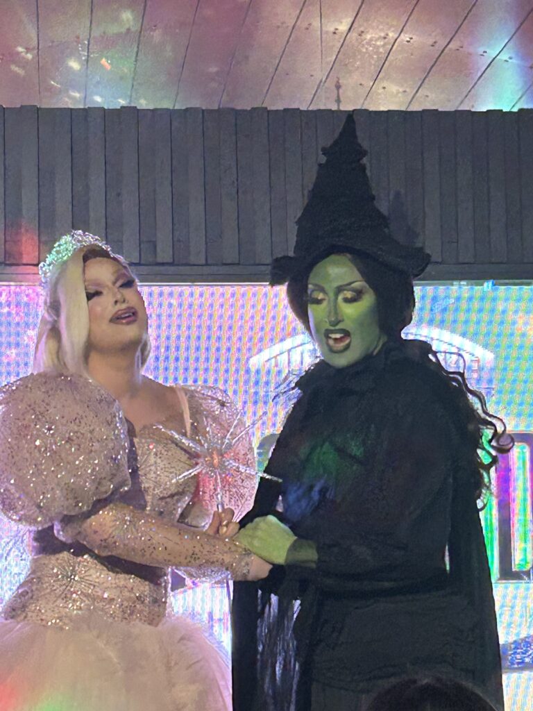 Drag queens Jan Sport and Jackie Cox perform on stage as Wicked characters Elphaba and Glinda.