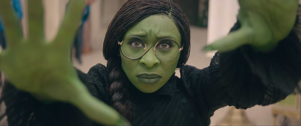 Elphaba, a woman who is green, holds her hands out in front of her as she practices magic.