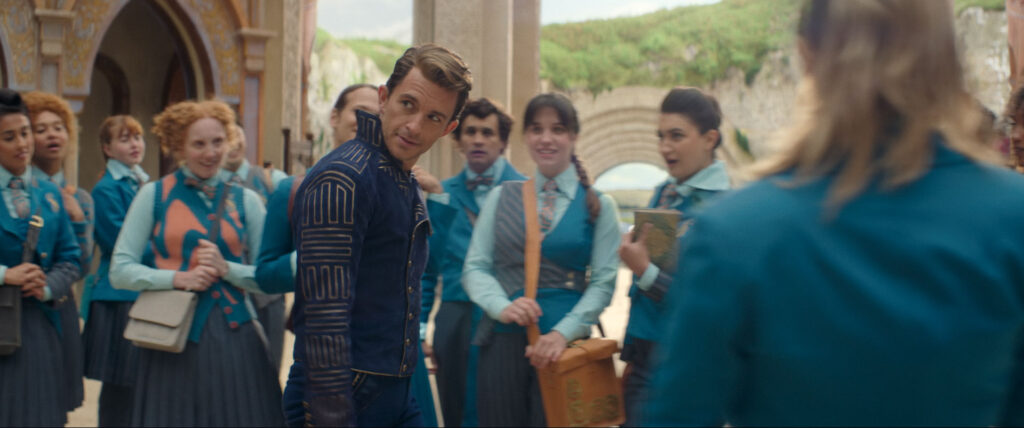 A group of students in Shiz University school uniforms stand transfixed as Prince Fiyero sings.