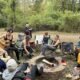 A group of women sit around a campfire in the woods.