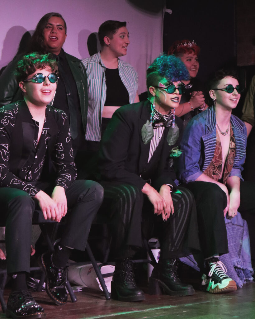 A group of butch performers watch the show on stage.