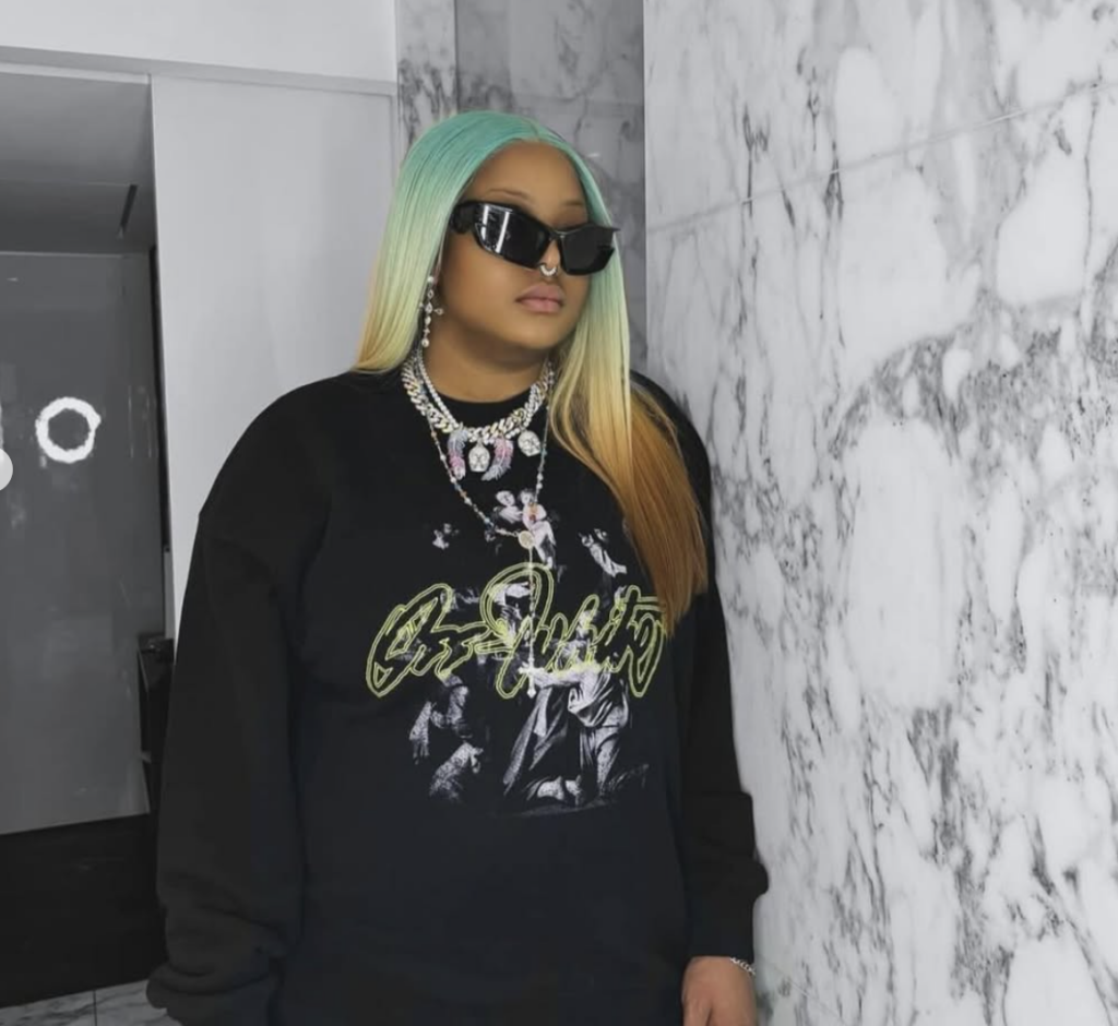 Brenda Biyaa wears shades over her eyes as she poses in a black graphic sweatshirt.