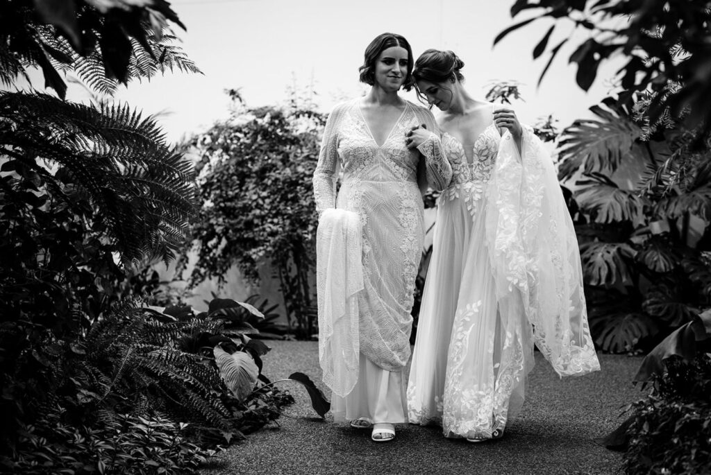 In a black and white photo, Zooey Zephyr and Erin Reed pose in white wedding dresses in a garden.