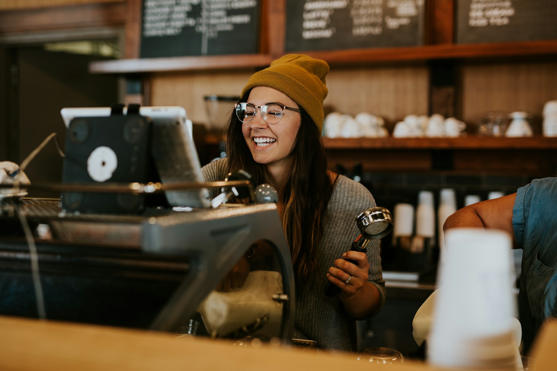 A woman smiles from behind the bar at a cafe.