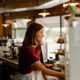 A woman smiles from behind the bar at a cafe.