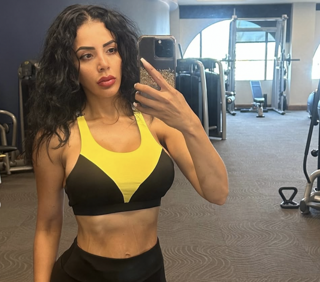 Jasmine Pineda has long curly black hair, and she takes a selfie as she stands in a gym.