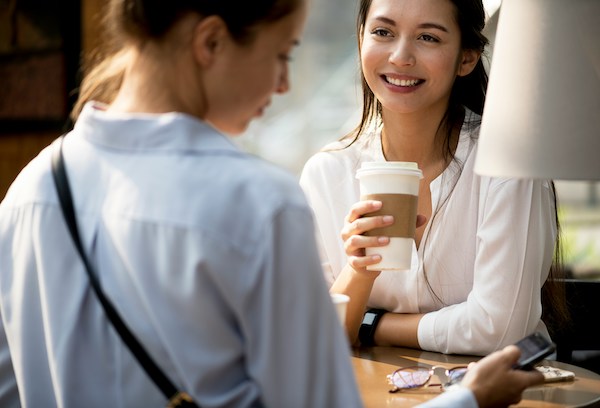 Two women sit across from one another at a table in a coffee shop.