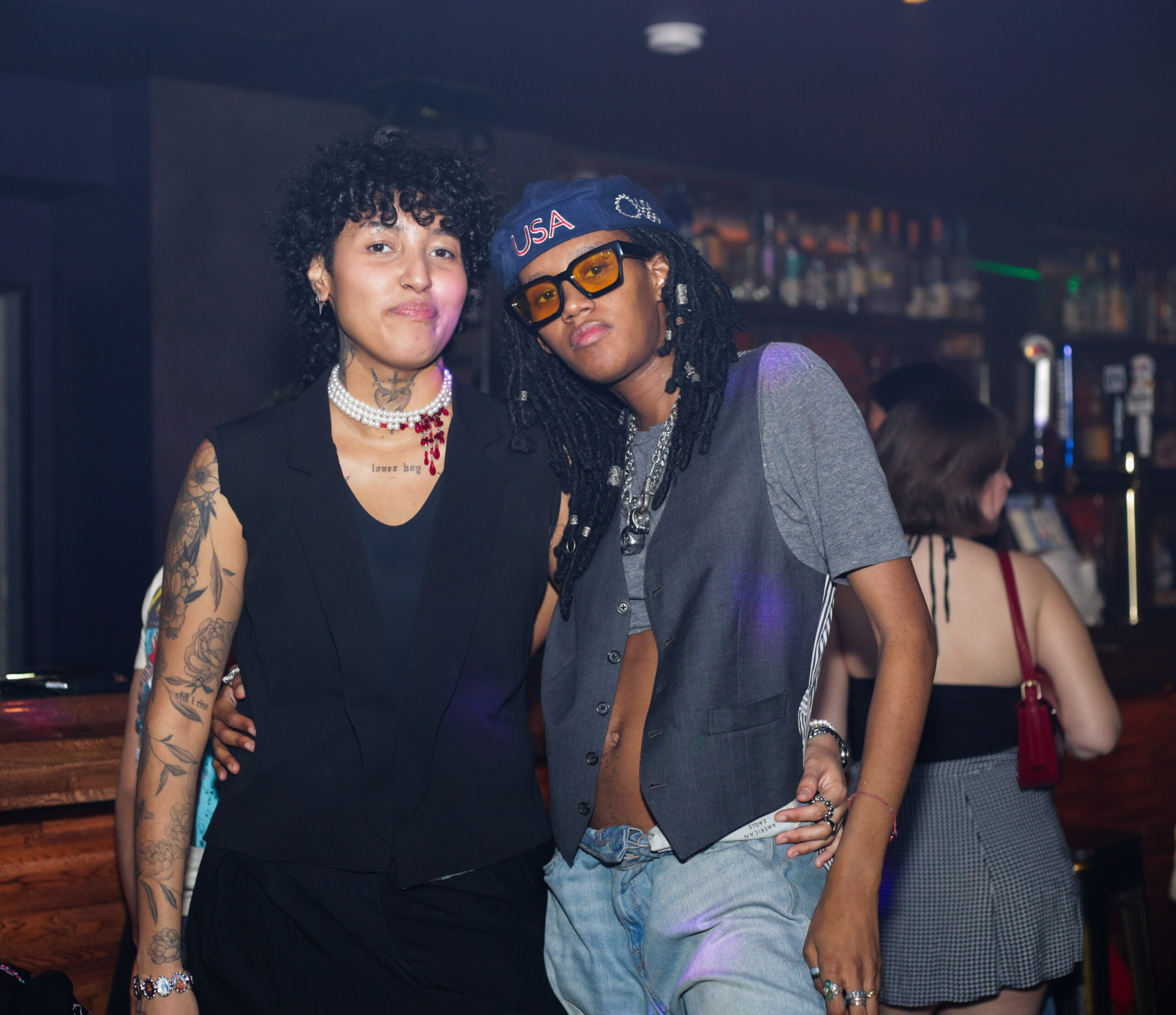 Two beautiful Black masc folks pose together, looking into the camera.