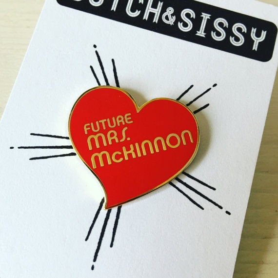 A red, heart-shaped enamel pin that says "Future Mrs. McKinnon" 