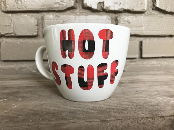 A white mug that says hot stuff in plaid bubble letters